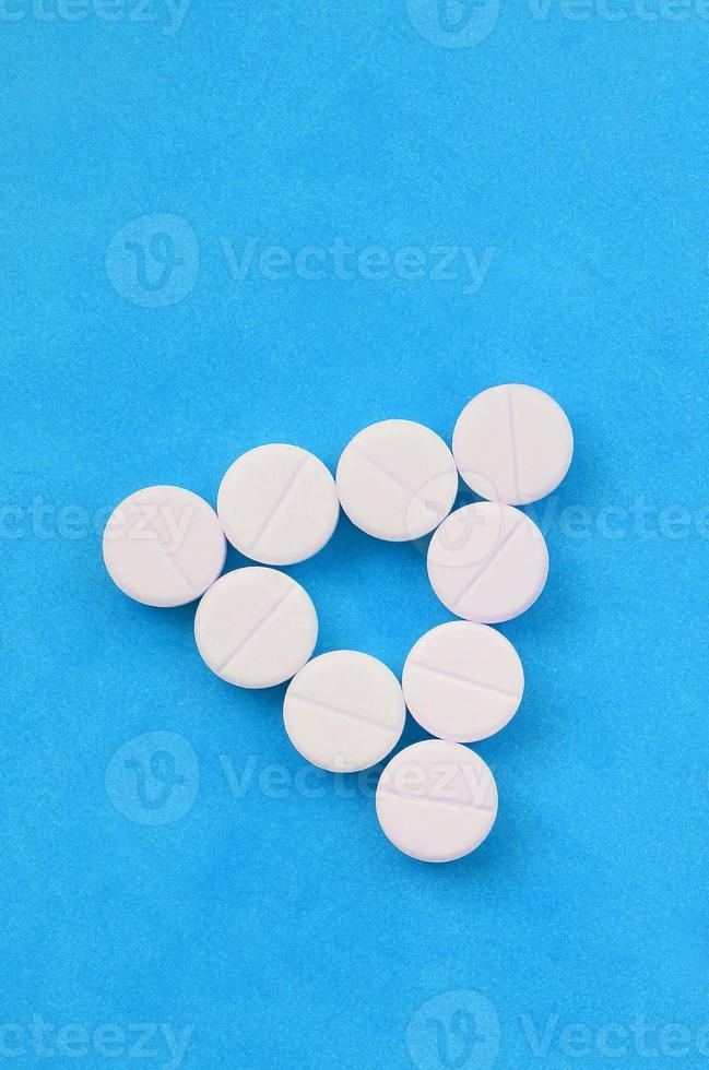 Several white tablets lie on a bright blue background in the form of an even triangle. Background image on medicine and pharmaceutical topics photo