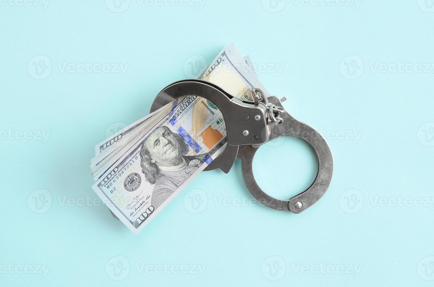 Silver police handcuffs and hundred dollar bills lies on light blue background photo