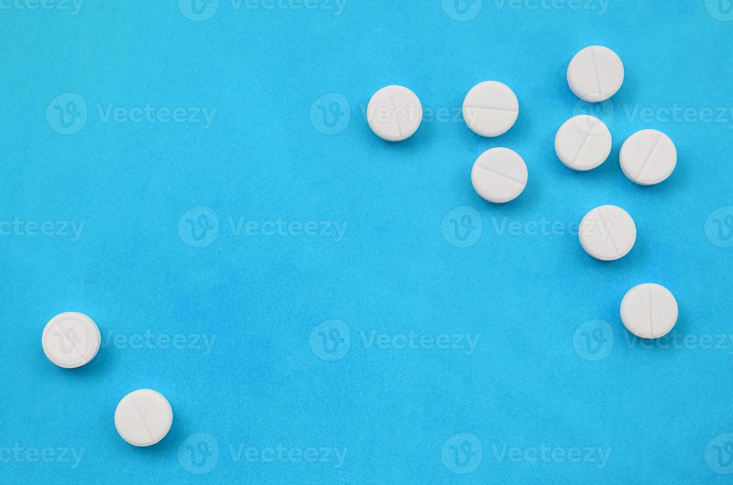 A few white tablets lie on a bright blue background surface. Background image on medical and pharmaceutical topics photo