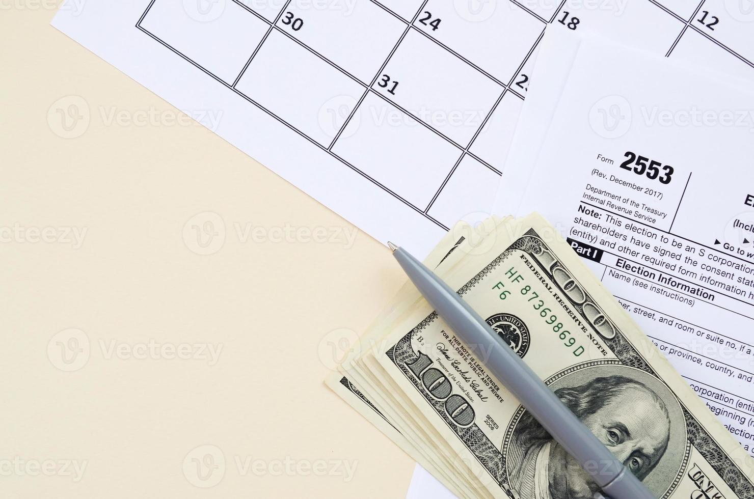 IRS Form 2553 Election by a Small Business Corporation tax blank lies with pen and many hundred dollar bills on calendar page photo
