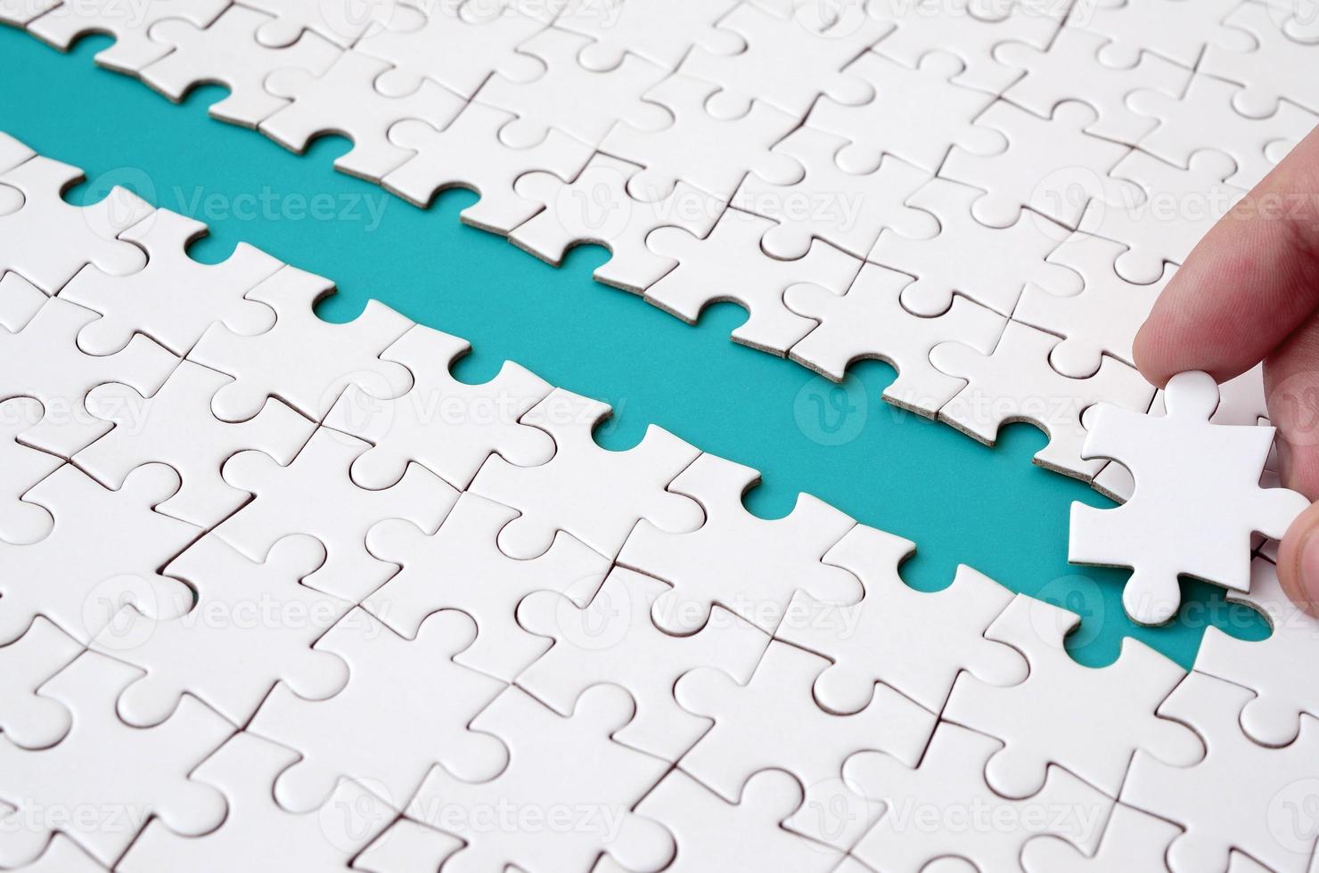 The human hand paves the way to the surface of the jigsaw puzzle, forming a blue space. The concept of overcoming the difficulties on the way to success photo