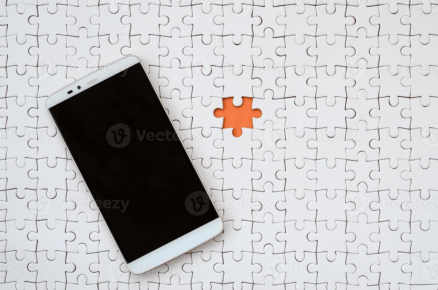 A modern big smartphone with a touch screen lies on a white jigsaw puzzle in an assembled state photo