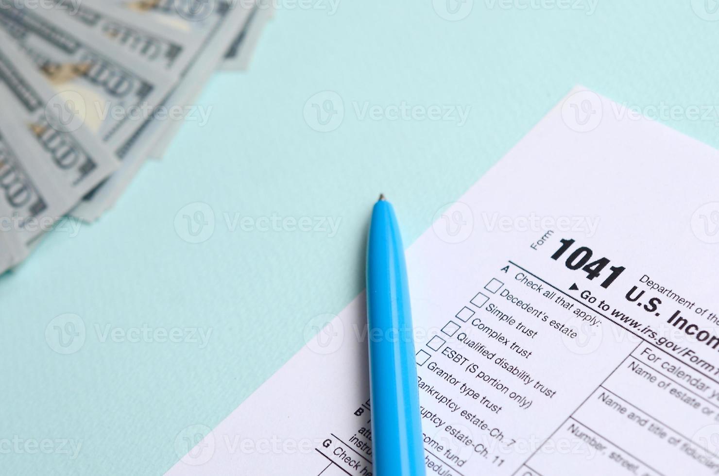 El formulario de impuestos 1041 se encuentra cerca de los billetes de cien dólares y el bolígrafo azul sobre un fondo azul claro. declaración de impuestos sobre la renta de estados unidos para sucesiones y fideicomisos foto