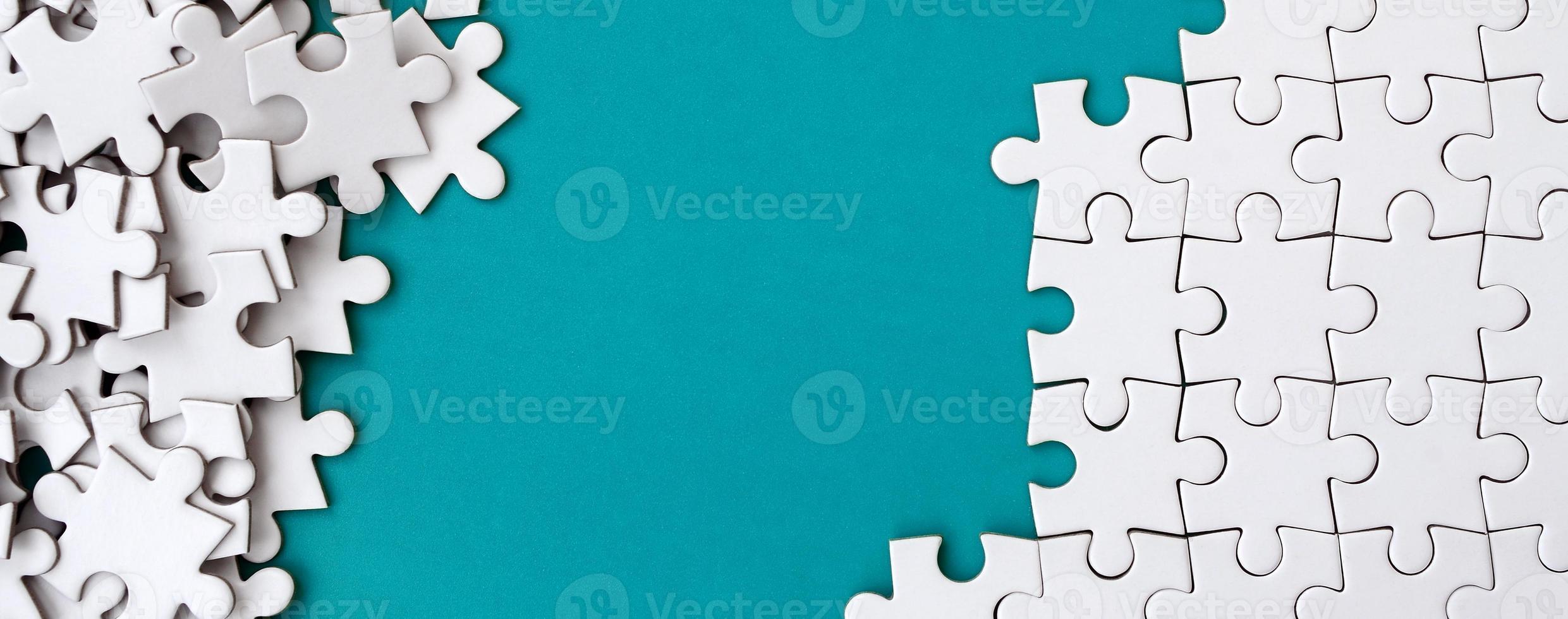 Fragment of a folded white jigsaw puzzle and a pile of uncombed puzzle elements against the background of a blue surface. Texture photo with space for text