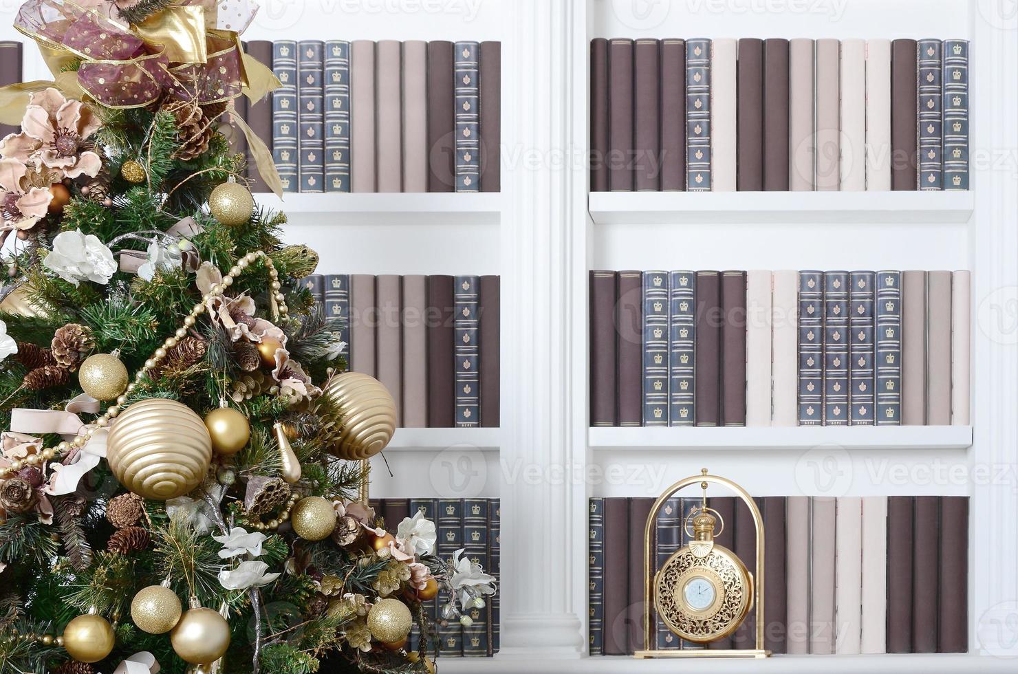 A beautiful decorated Christmas tree on the background of a bookshelf with many books of different colors and golden clock. Christmas background image of the library photo