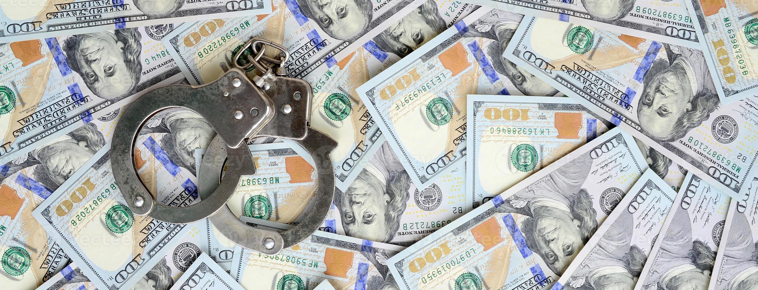 Silver police handcuffs lies on a many dollar bills photo