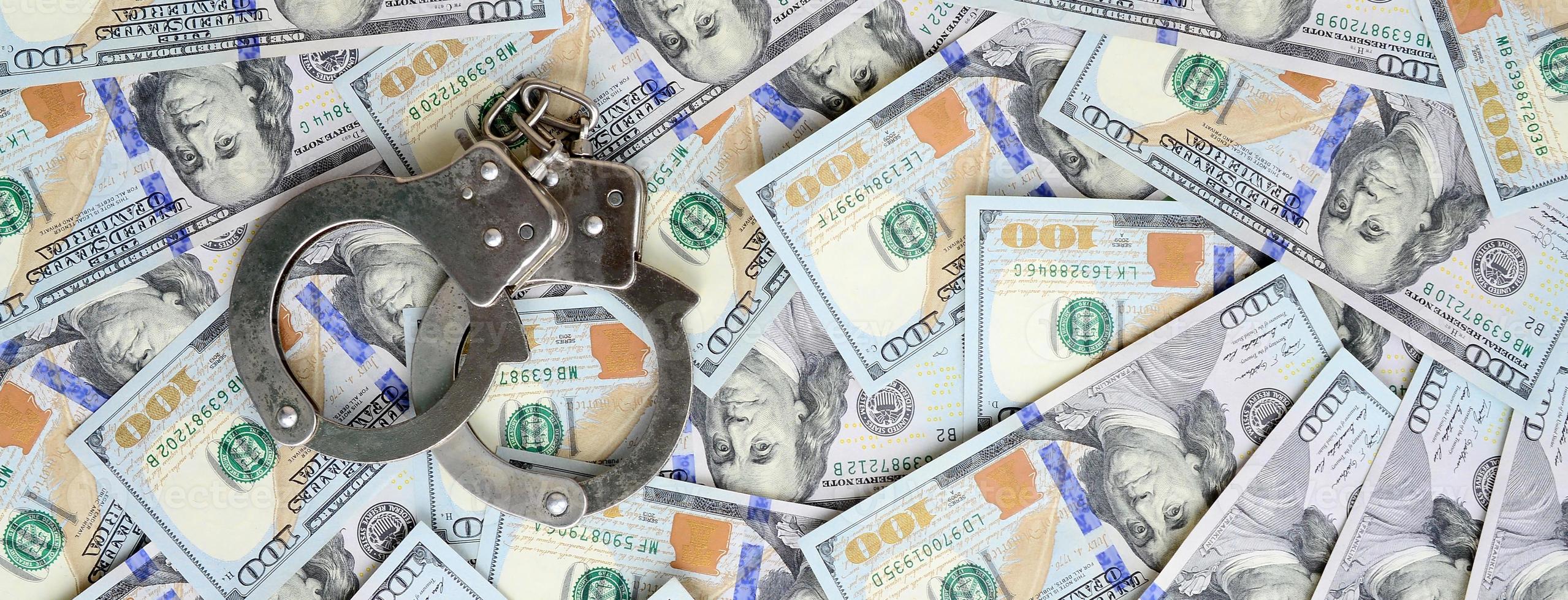 Silver police handcuffs lies on a many dollar bills photo