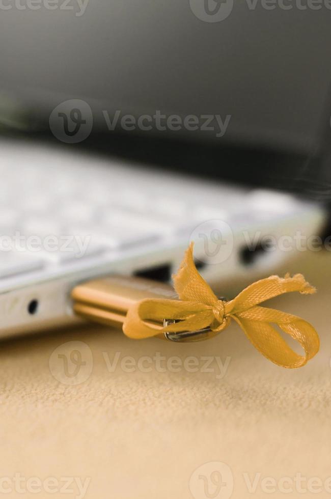 una unidad flash usb naranja con un lazo está conectada a una computadora portátil blanca, que se encuentra sobre una manta de tela suave y esponjosa de color naranja claro. diseño femenino clásico para una tarjeta de memoria foto