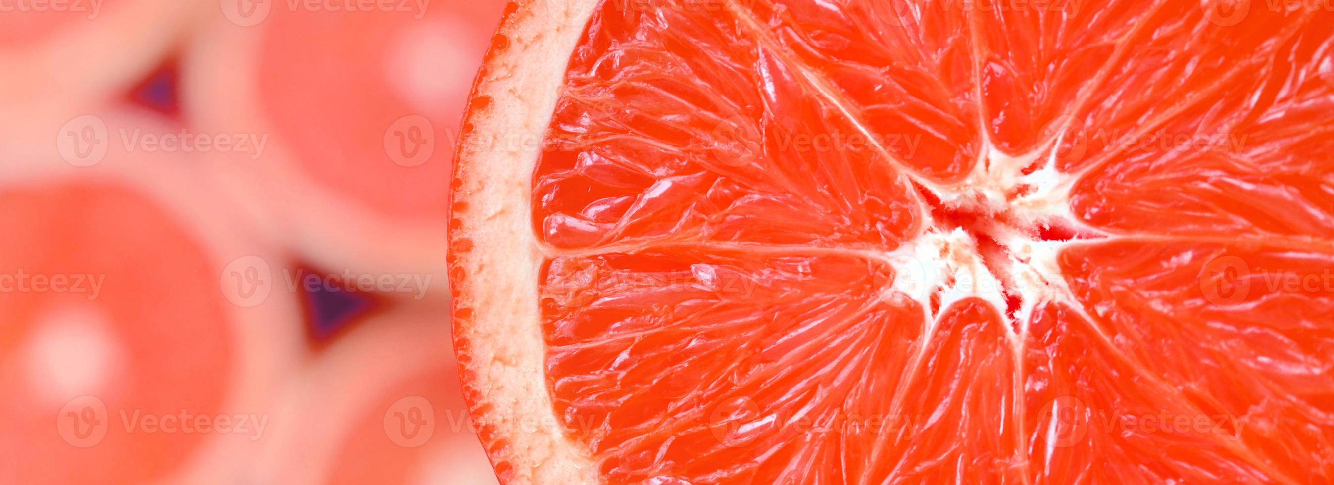 Top view of a fragment of the red grapefruit slice on the background of many blurred grapefruit slices. A saturated citrus texture image photo