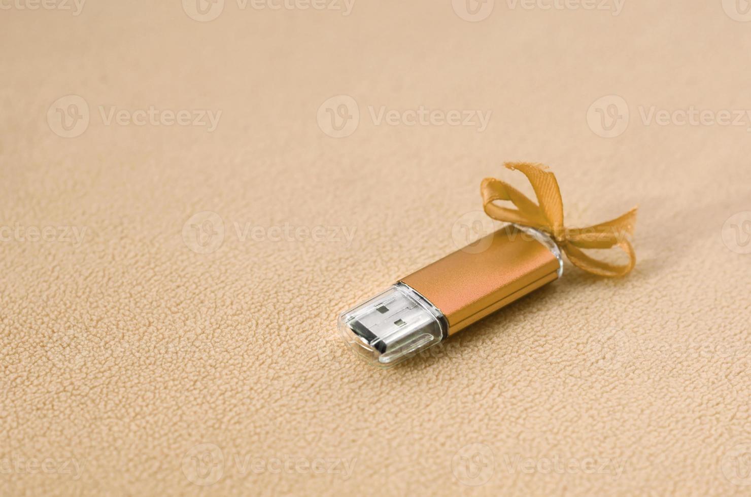 Orange usb flash memory card with a blue bow lies on a blanket of soft and furry light orange fleece fabric. Classic female gift design for a memory card photo