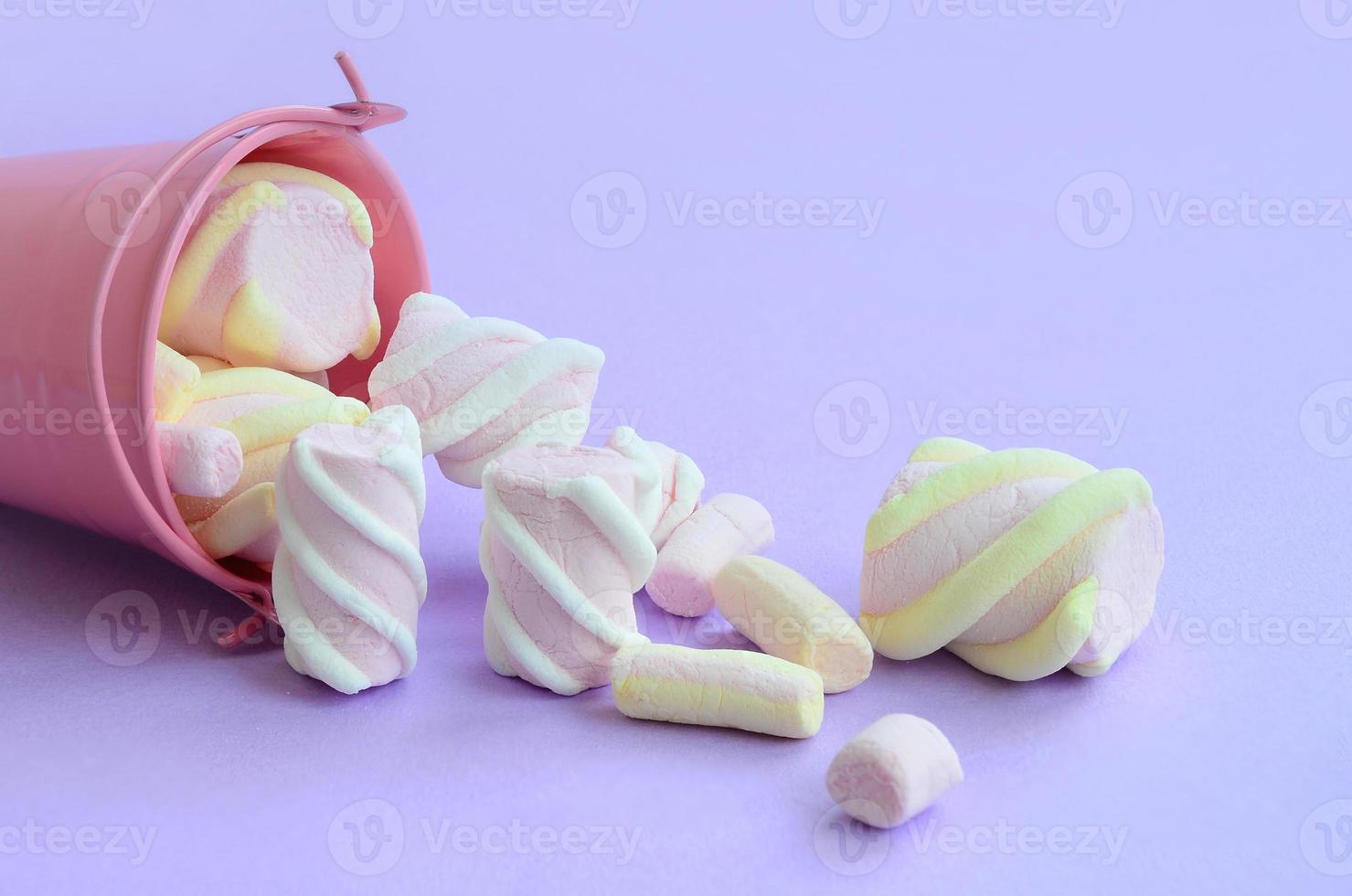 Overturned miniature pink bucket filled with marshmallow lies on a purple pastel background. Minimal concept photo