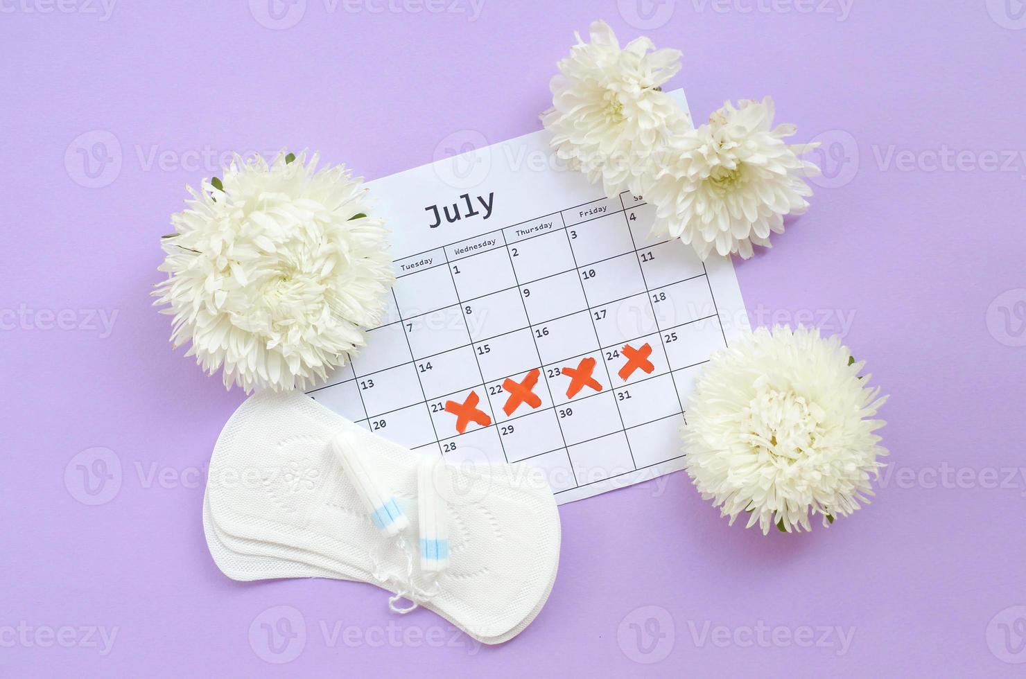 almohadillas menstruales y tampones en el calendario del período de menstruación con flores blancas sobre fondo lila foto