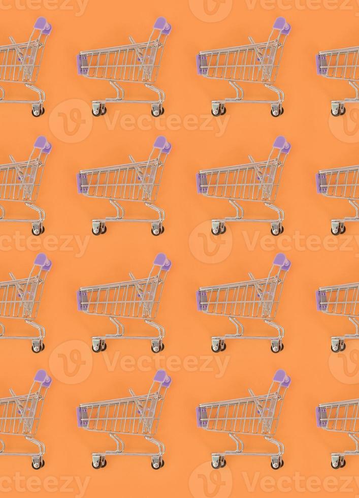 Shopping addiction, shopping lover or shopaholic concept. Many small empty shopping carts perform a pattern on a pastel colored paper background. Flat lay composition, top view photo