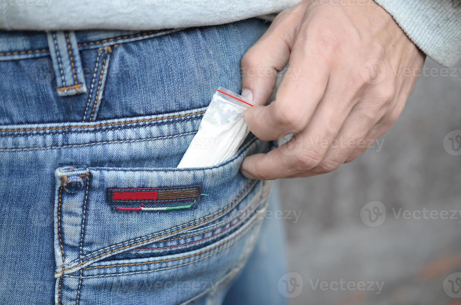 Male hand retrieving drug packet our of blue jean pocket with copy space on abandoned building background photo