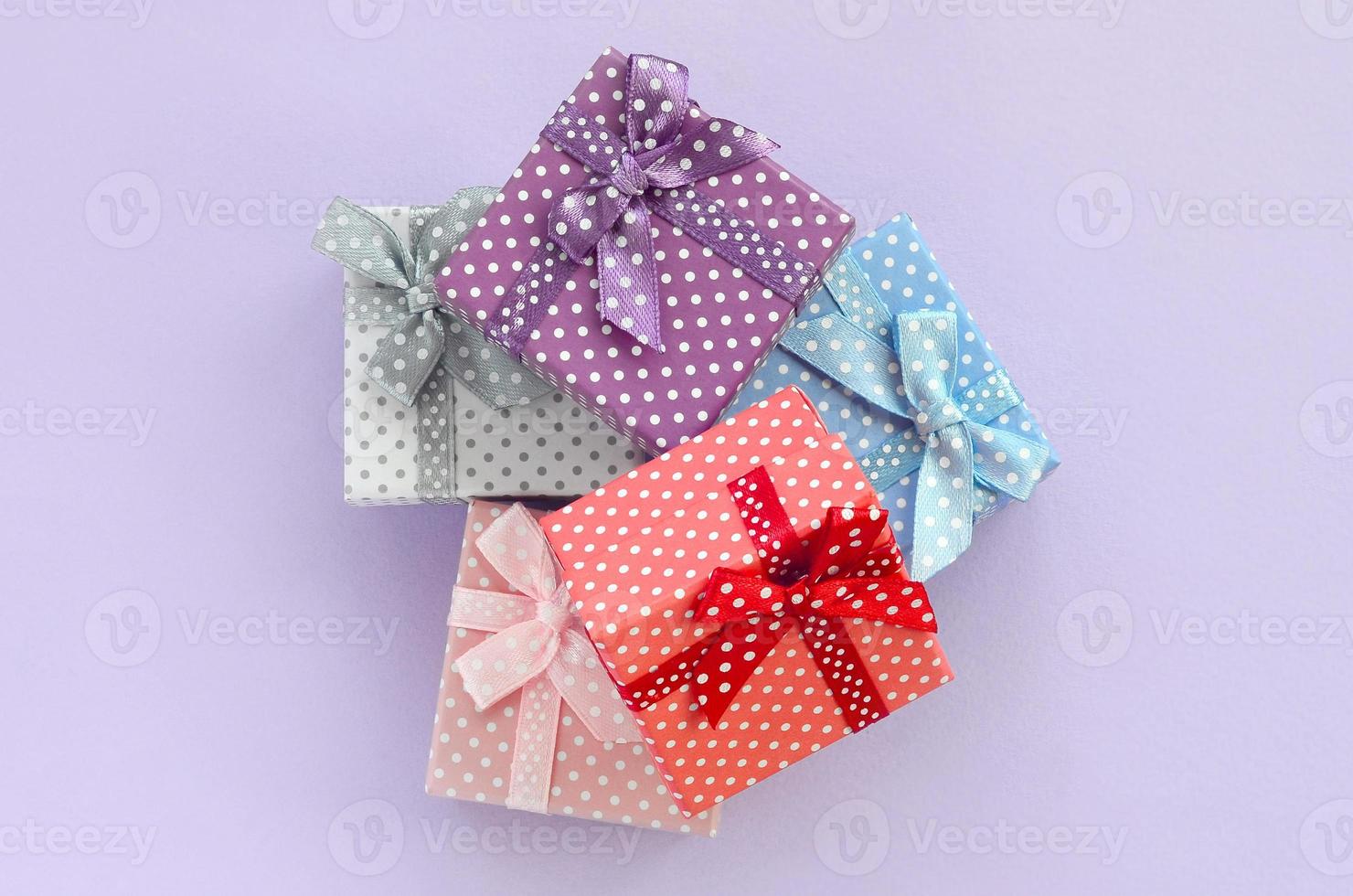Pile of a small colored gift boxes with ribbons lies on a violet background. Minimalism flat lay top view photo