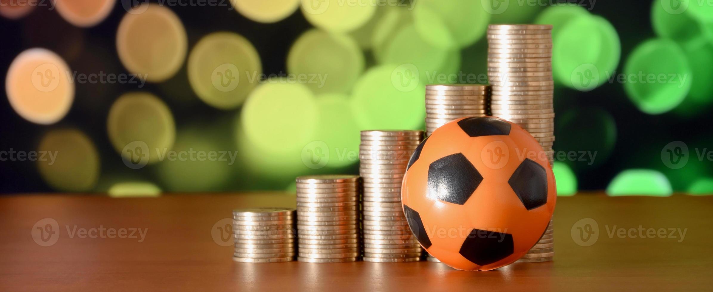 pelota de fútbol y montones de monedas de oro en el gráfico de crecimiento en el fondo borroso del bokeh foto