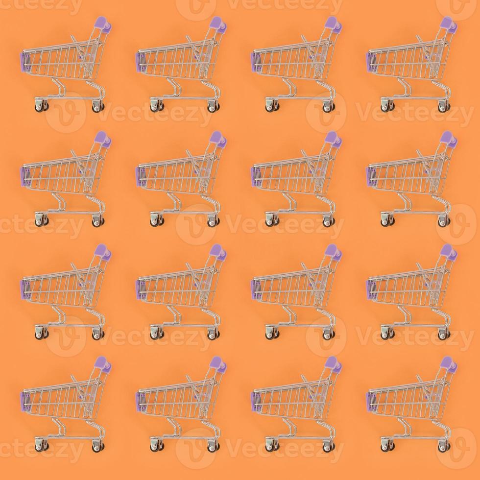 Shopping addiction, shopping lover or shopaholic concept. Many small empty shopping carts perform a pattern on a pastel colored paper background. Flat lay composition, top view photo