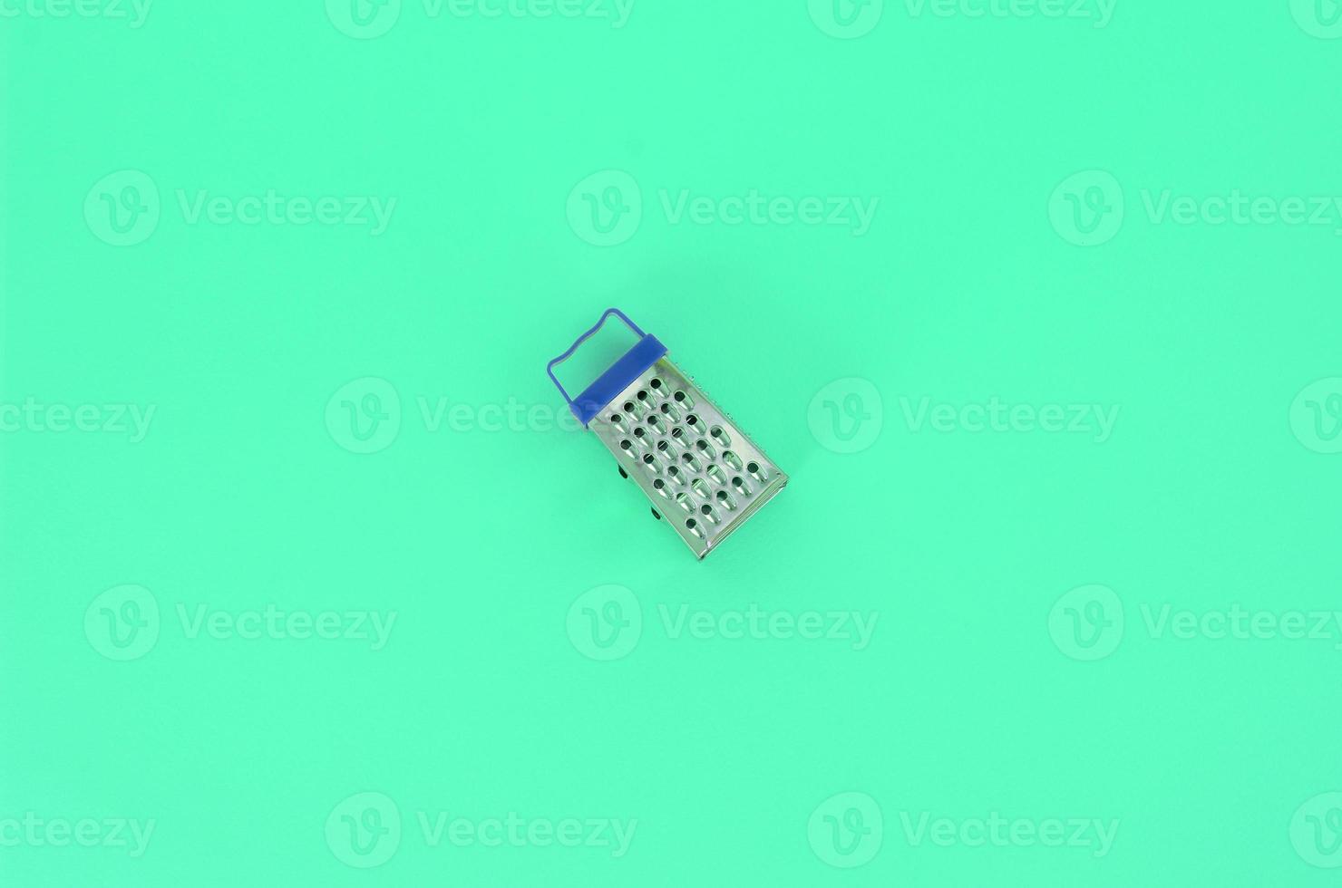 Stainless steel grater lies on a pastel colored paper. Kitchen accessories. Tools for cooking. Flat lay top view photo