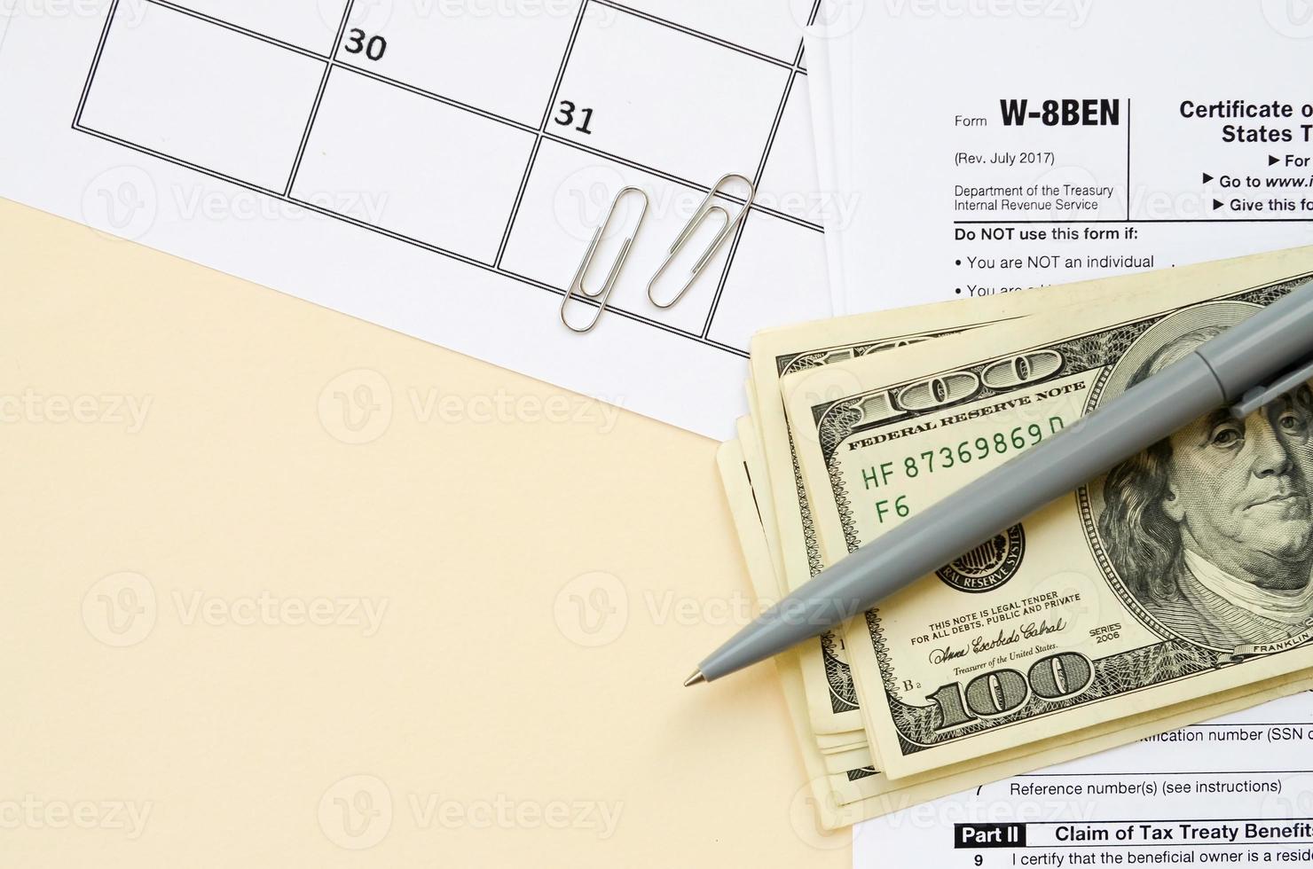 IRS Form W-8BEN Certificate of foreign status of beneficial owner for United States tax withholding and reporting for individuals blank lies with pen and hundred dollar bills on calendar page photo