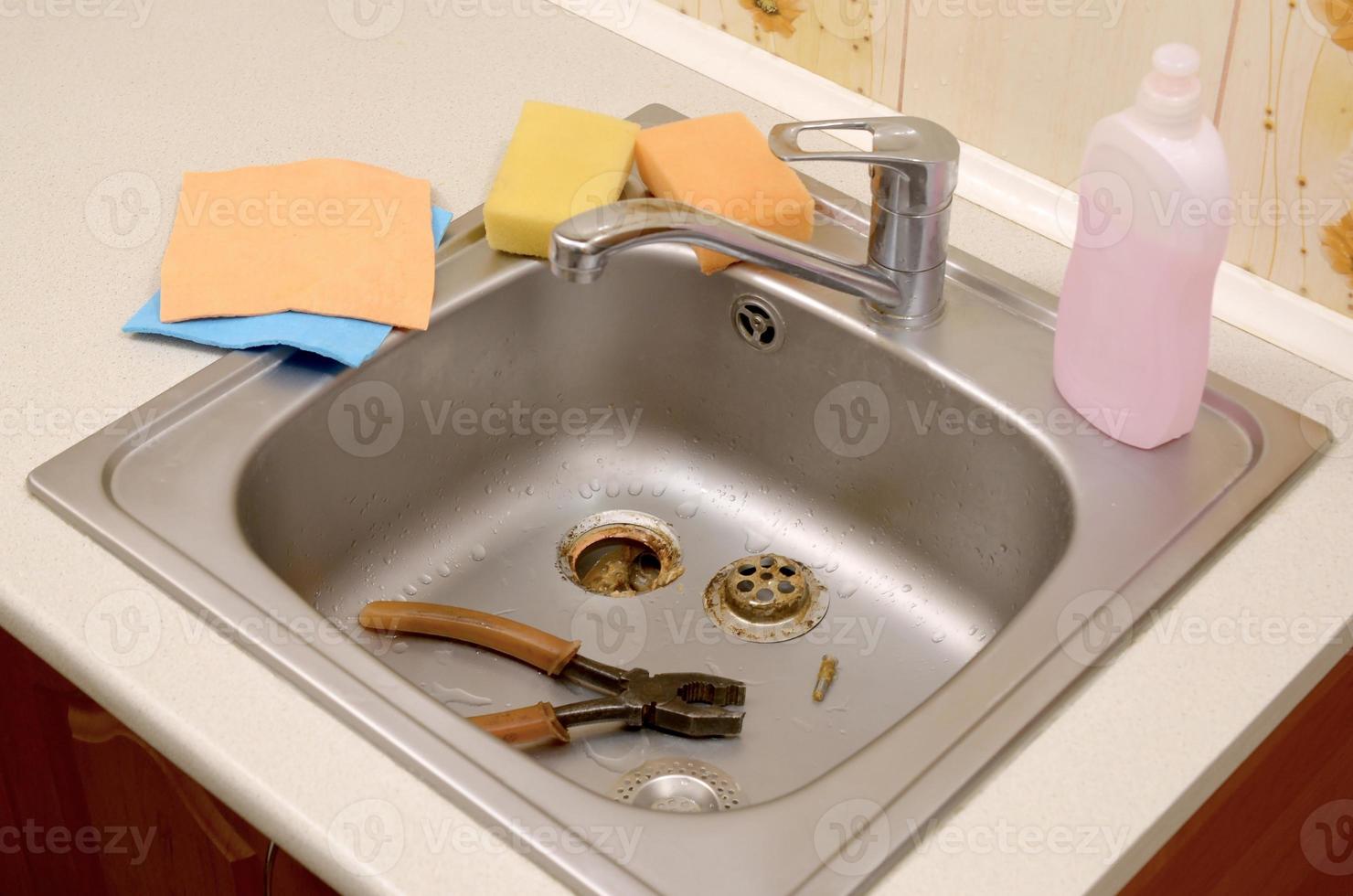 Pliers inside the silvery kitchen sink with a disassembled protective filter photo