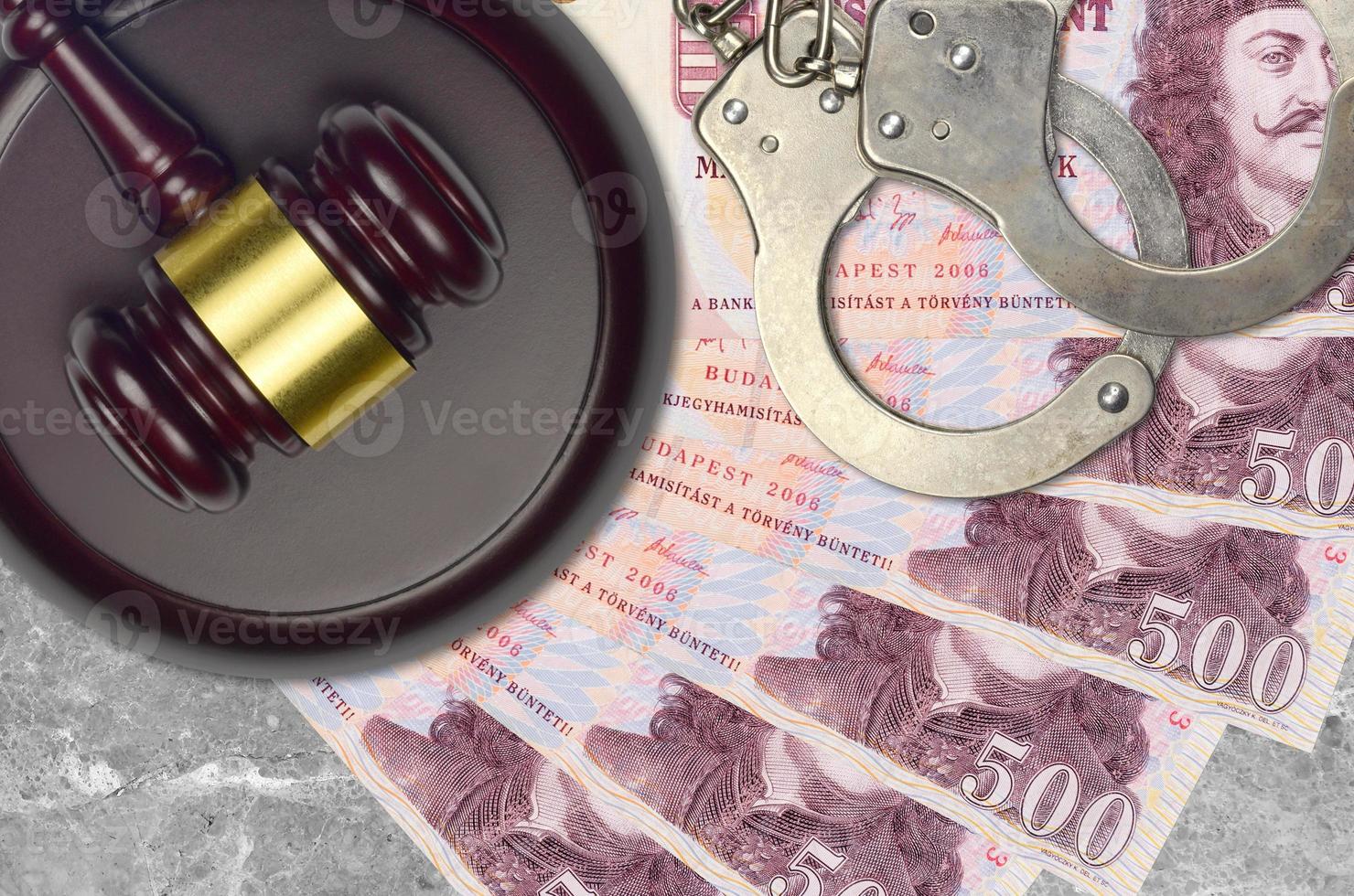 500 Hungarian forint bills and judge hammer with police handcuffs on court desk. Concept of judicial trial or bribery. Tax avoidance photo