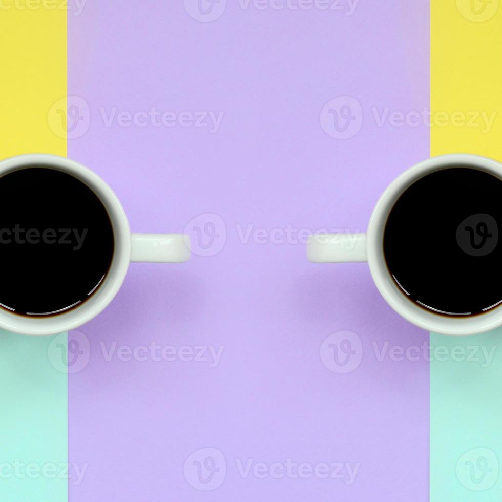 Two small white coffee cups on texture background of fashion pastel blue, yellow, violet and pink colors paper in minimal concept photo