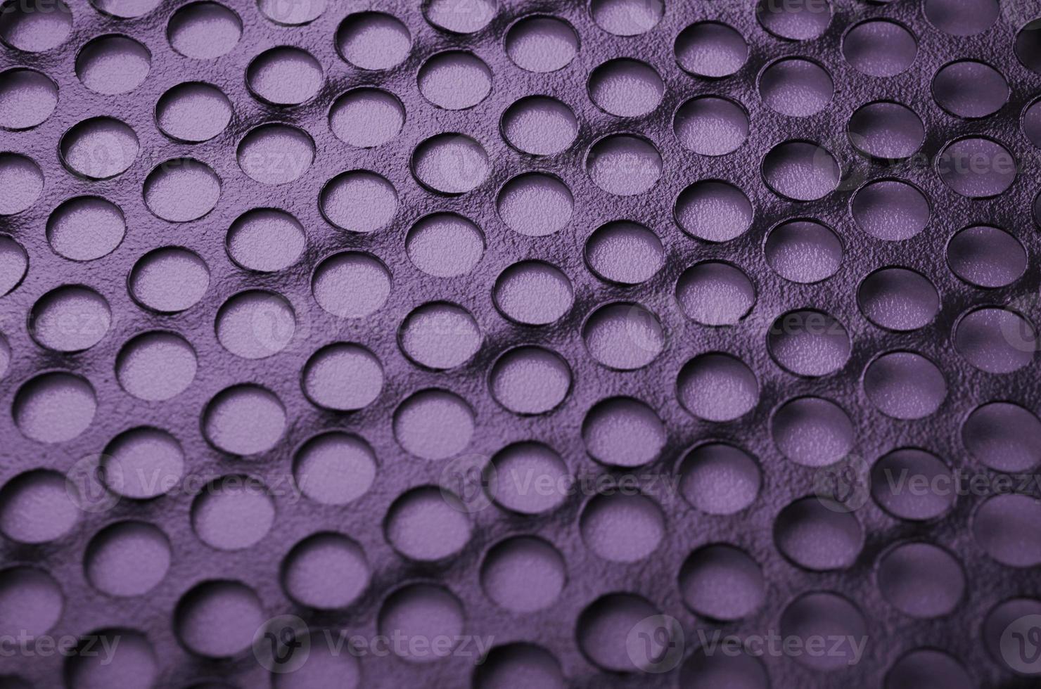 Black metal computer case panel mesh with holes on purple background. Abstract close up photo
