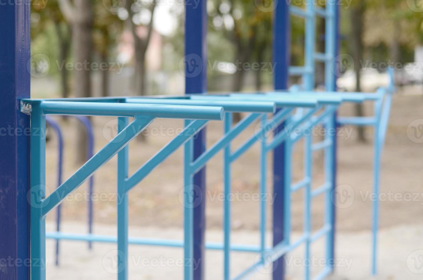 Blue metal pipes and cross-bars against a street sports field for training in athletics. Outdoor athletic gym equipment. Macro photo with selective focus and extremely blurred background