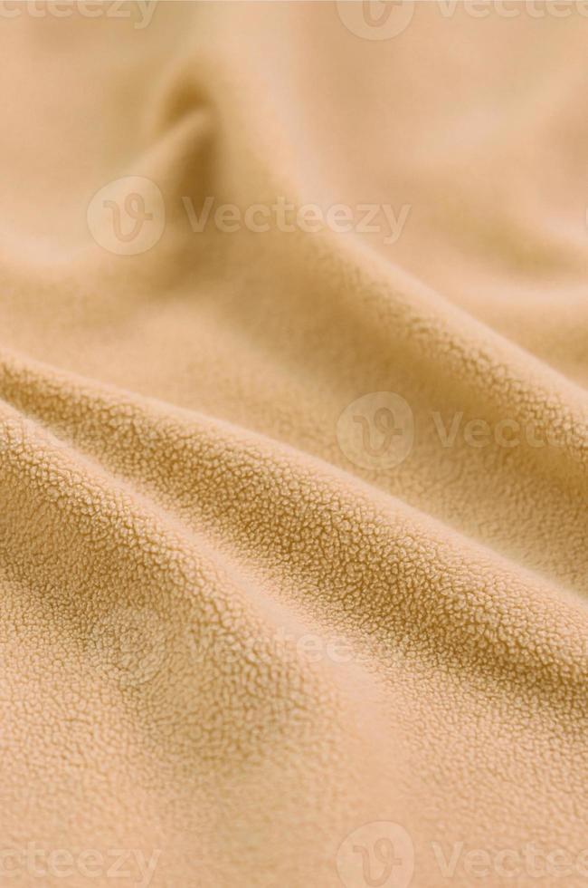 The blanket of furry orange fleece fabric. A background of light orange soft plush fleece material with a lot of relief folds photo