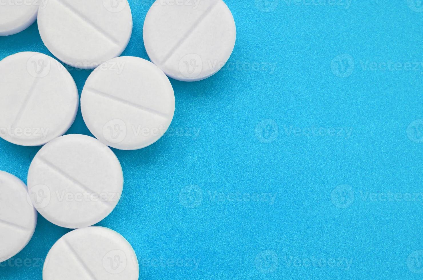 A few white tablets lie on a bright blue background surface. Background image on medical and pharmaceutical topics photo