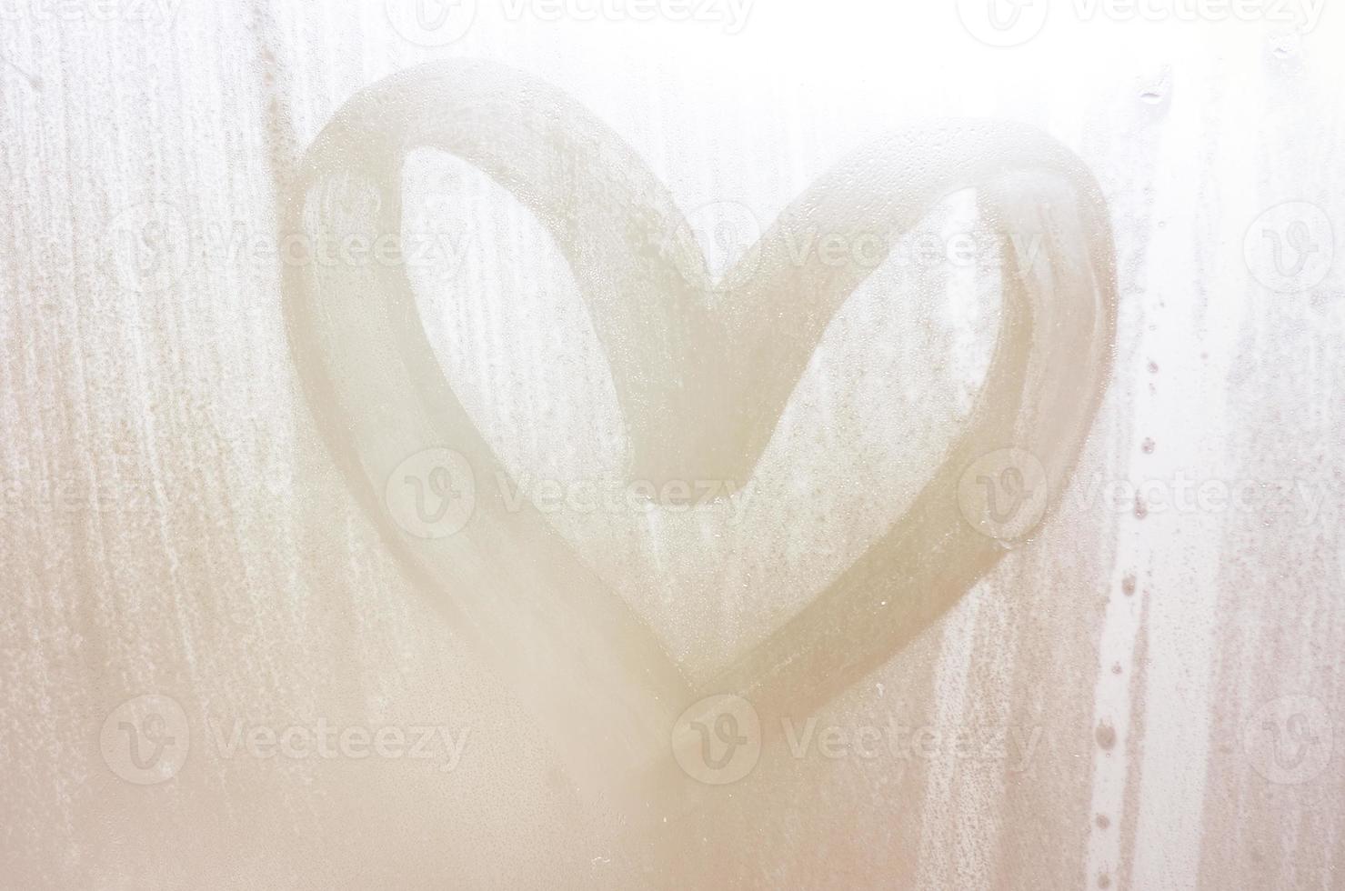 A heart-shaped drawing drawn by a finger on a misted glass in rainy weather photo