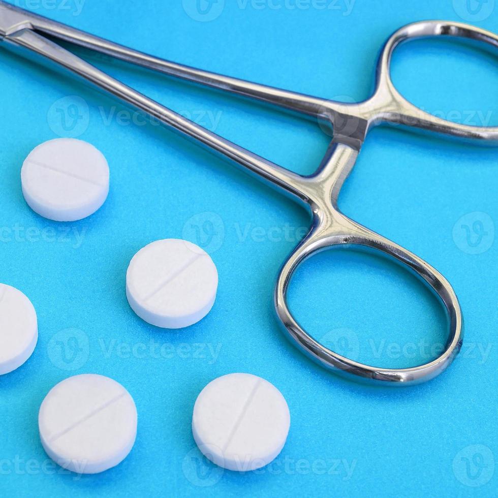Several white tablets and a medical clamp lie on a bright blue background surface. Background image on medical and pharmaceutical topics photo