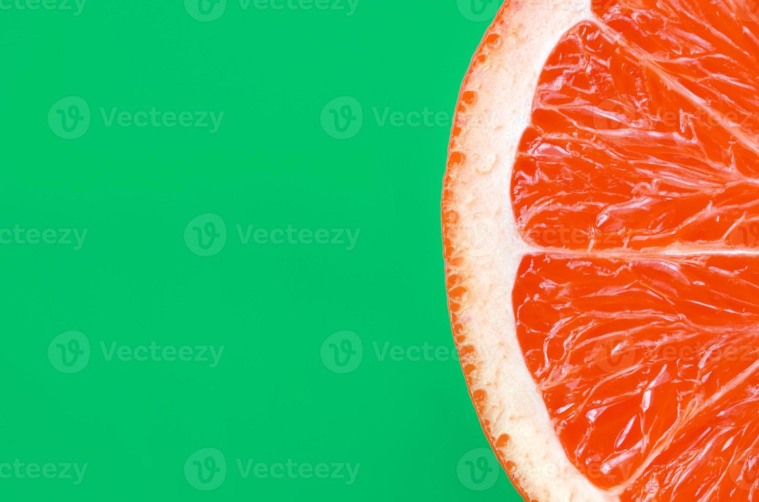 vista superior de una rodaja de pomelo sobre fondo brillante en color verde. una imagen de textura cítrica saturada foto