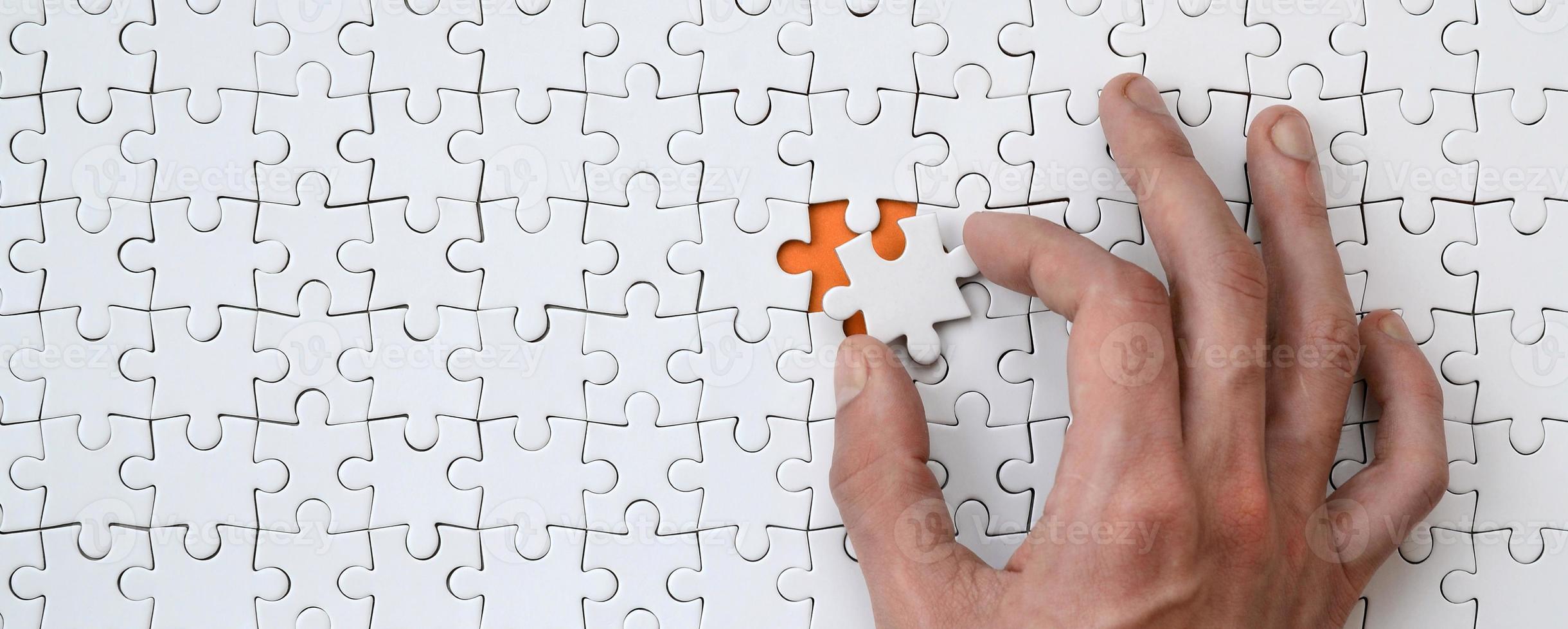 The texture of a white jigsaw puzzle in the assembled state with one missing element that the male hand puts in photo