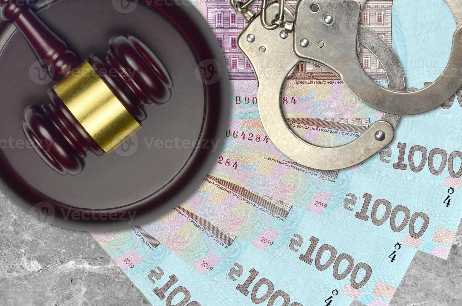 1000 Ukrainian hryvnias bills and judge hammer with police handcuffs on court desk. Concept of judicial trial or bribery. Tax avoidance photo
