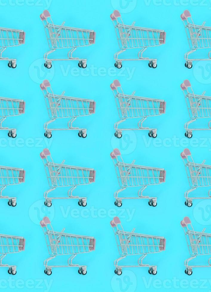 Shopping addiction, shopping lover or shopaholic concept. Many small empty shopping carts perform a pattern on a pastel colored paper background. Flat lay composition, top view photo