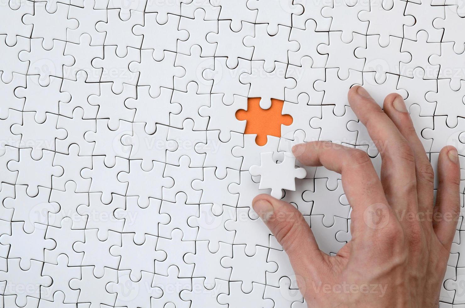 The texture of a white jigsaw puzzle in the assembled state with one missing element that the male hand puts in photo