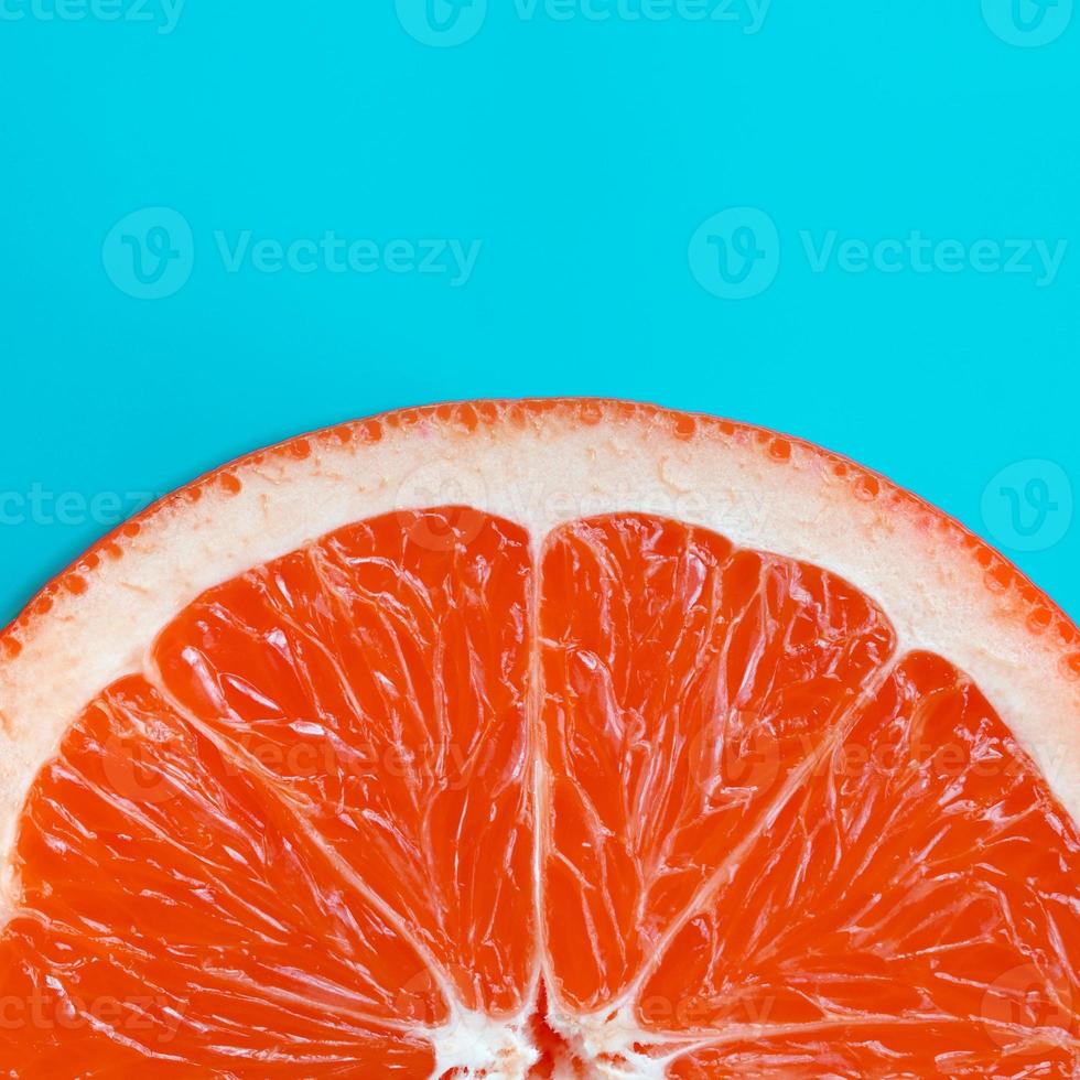 Top view of an one grapefruit slice on bright background in blue color. A saturated citrus texture image photo