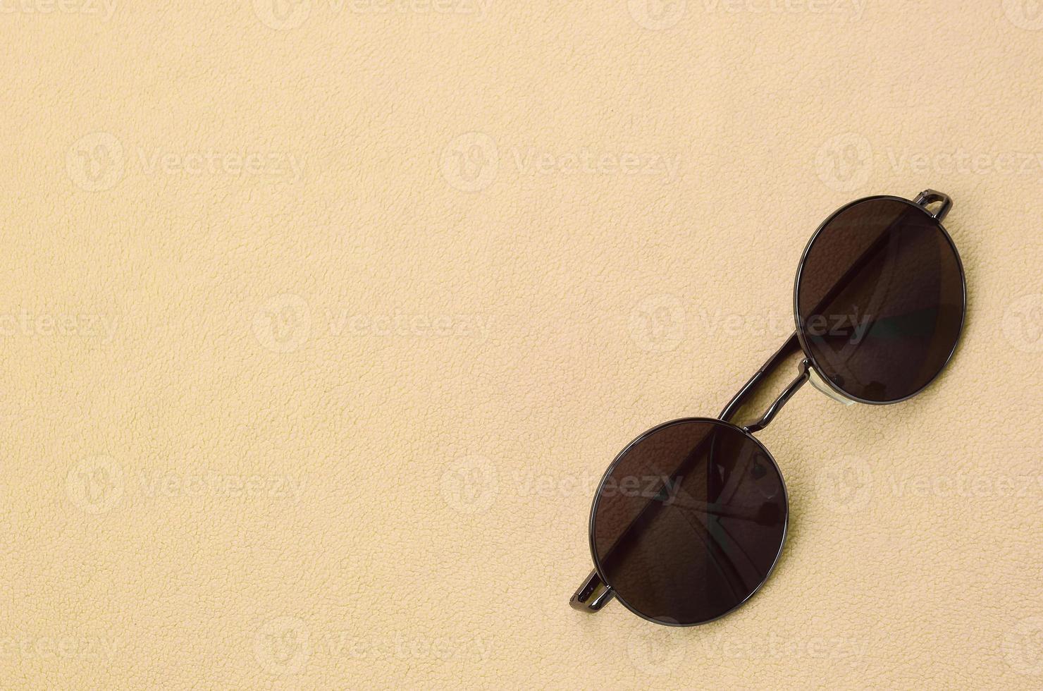 Stylish black sunglasses with round glasses lies on a blanket made of soft and fluffy light orange fleece fabric. Fashionable background picture in fashion colors photo