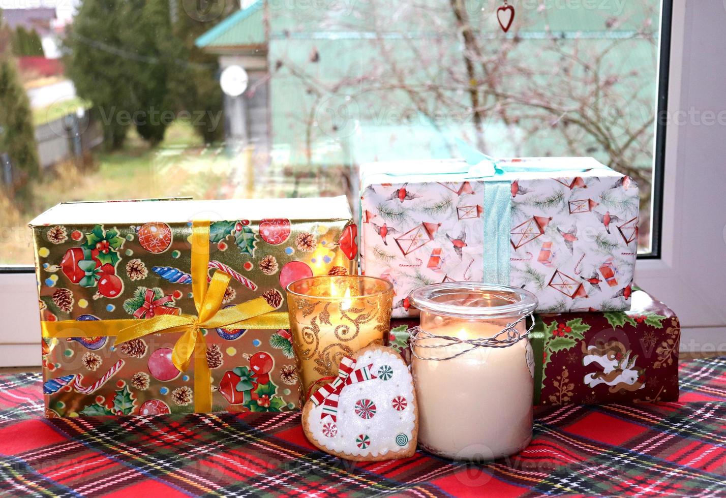 Christmas candles and festive boxes with gifts near window photo