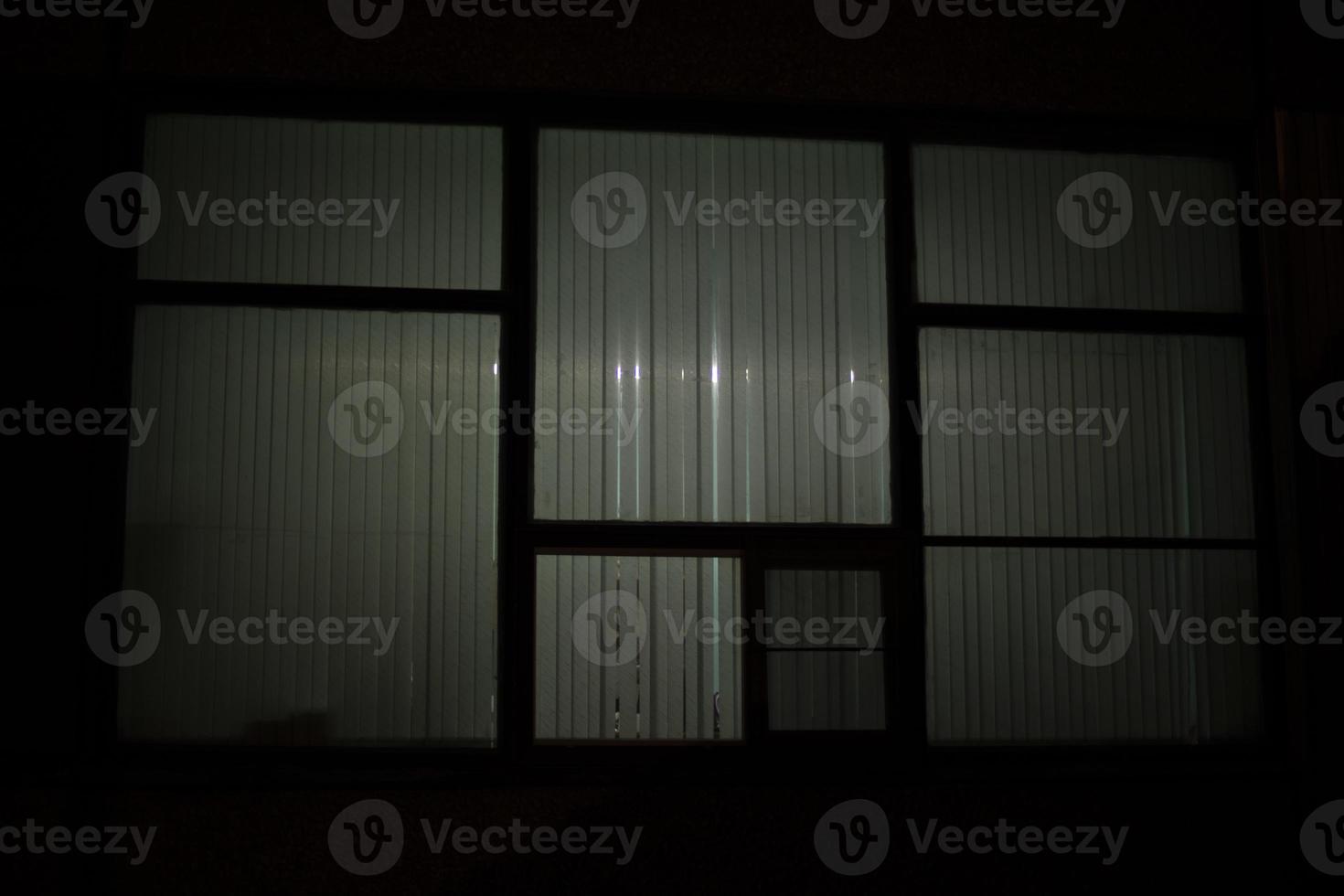 Big window at night. Window in building. Blinds cover light of lamp. photo