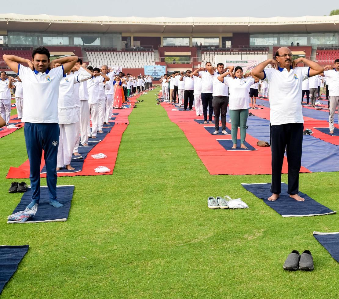 nueva delhi, india, 21 de junio de 2022 - sesión grupal de ejercicios de yoga para personas en el complejo deportivo yamuna en delhi el día internacional del yoga, gran grupo de adultos que asisten a clases de yoga en el estadio de cricket foto