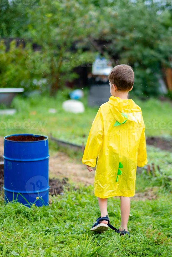 un niño con un impermeable amarillo camina bajo la lluvia, vista trasera. un niño en la calle. ropa brillante. caminar en la lluvia. foto