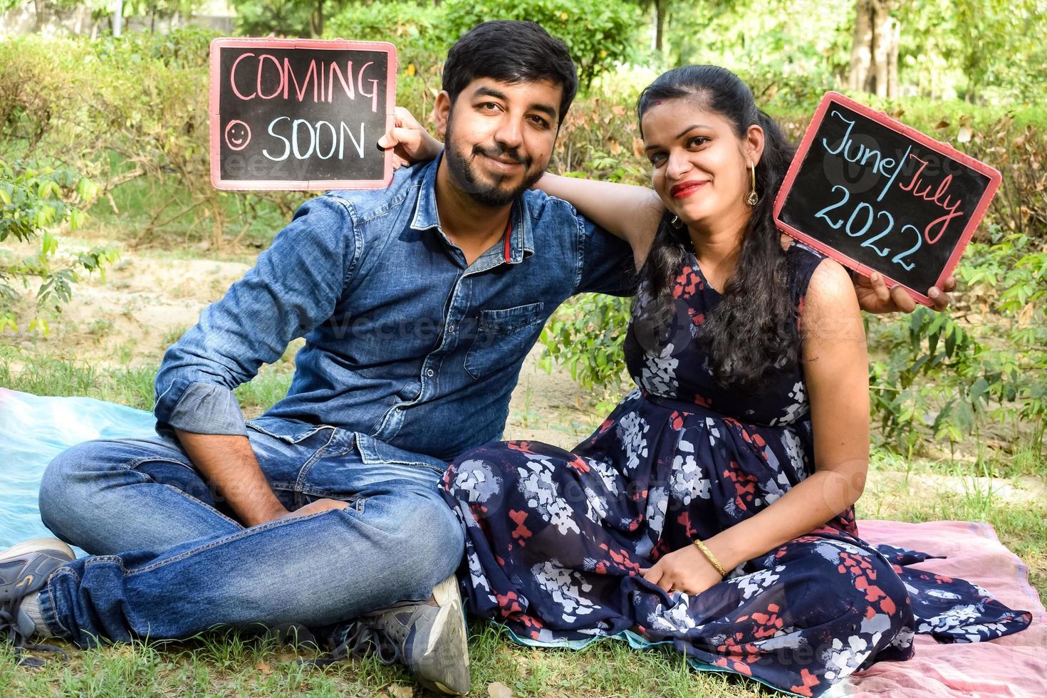 Indian couple posing for maternity baby shoot. The couple is posing in a lawn with green grass and the woman is falunting her baby bump in Lodhi Garden in New Delhi, India photo