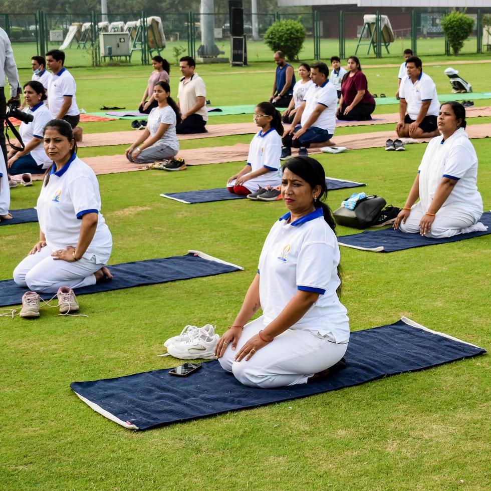 nueva delhi, india, 21 de junio de 2022 - sesión grupal de ejercicios de yoga para personas en el complejo deportivo yamuna en delhi el día internacional del yoga, gran grupo de adultos que asisten a clases de yoga en el estadio de cricket foto