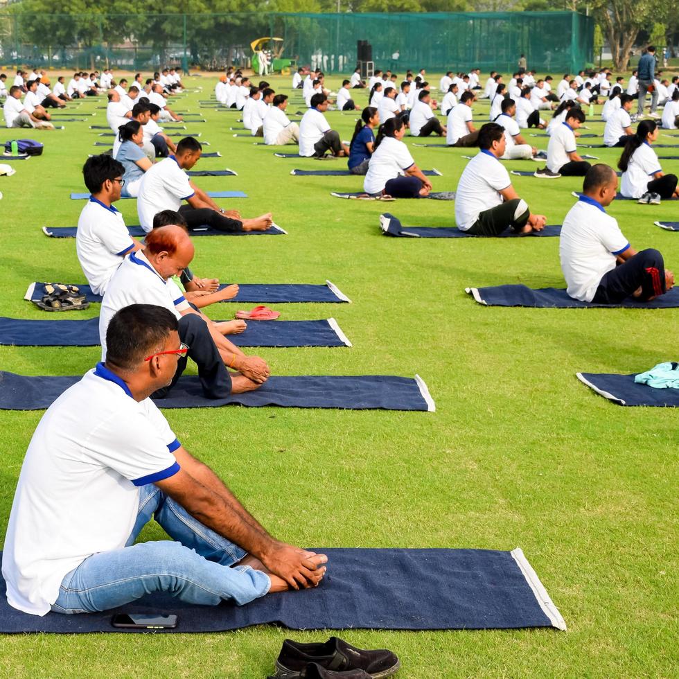 nueva delhi, india, 21 de junio de 2022 - sesión grupal de ejercicios de yoga para personas en el complejo deportivo yamuna en delhi el día internacional del yoga, gran grupo de adultos que asisten a clases de yoga en el estadio de cricket foto