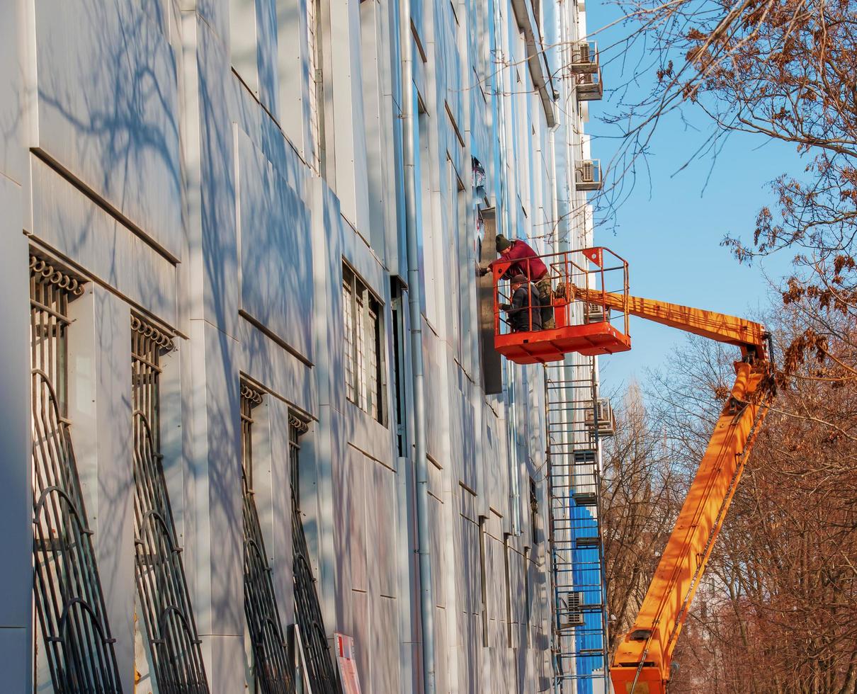 dnepropetrovsk, ucrania - 02.09.2022 constructor en una cesta de grúa repara el revestimiento de una estructura metálica en la pared de la fachada de un edificio. foto