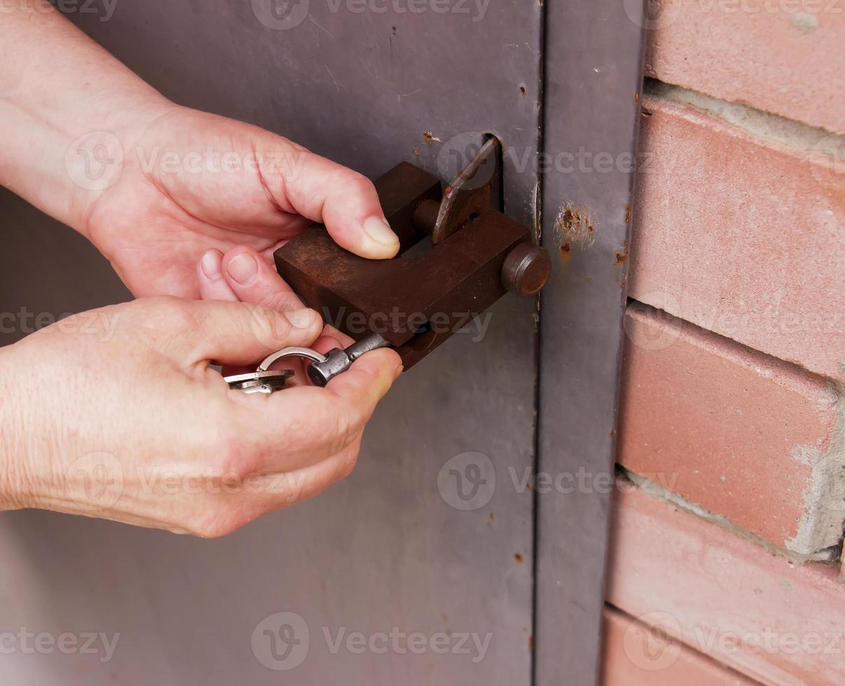 Women's hands open a rusty lock with keys. Lock on a metal door. Security. photo