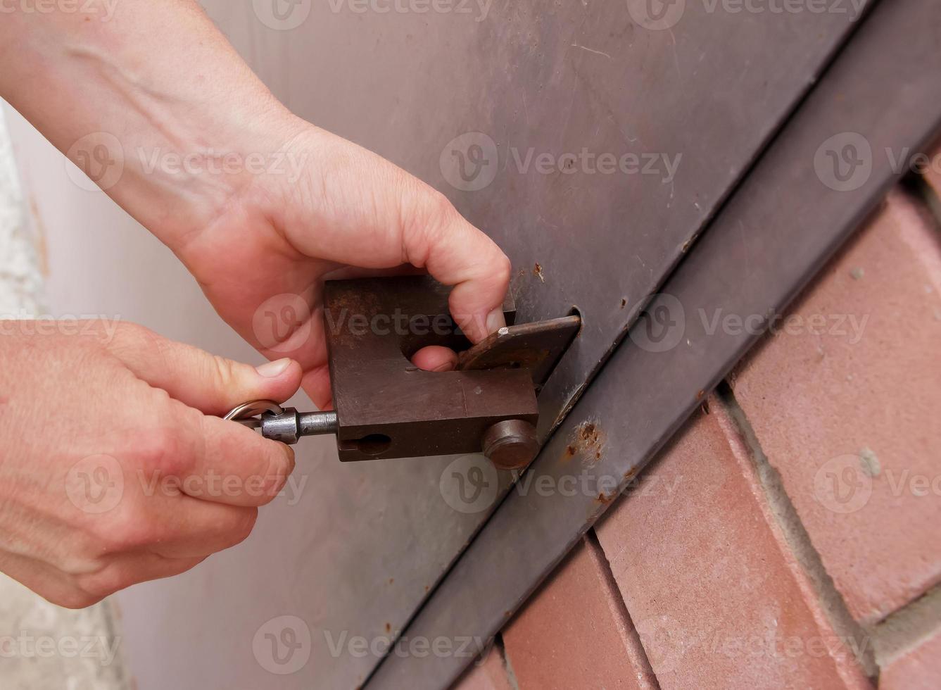 Women's hands open a rusty lock with keys. Lock on a metal door. Security. photo
