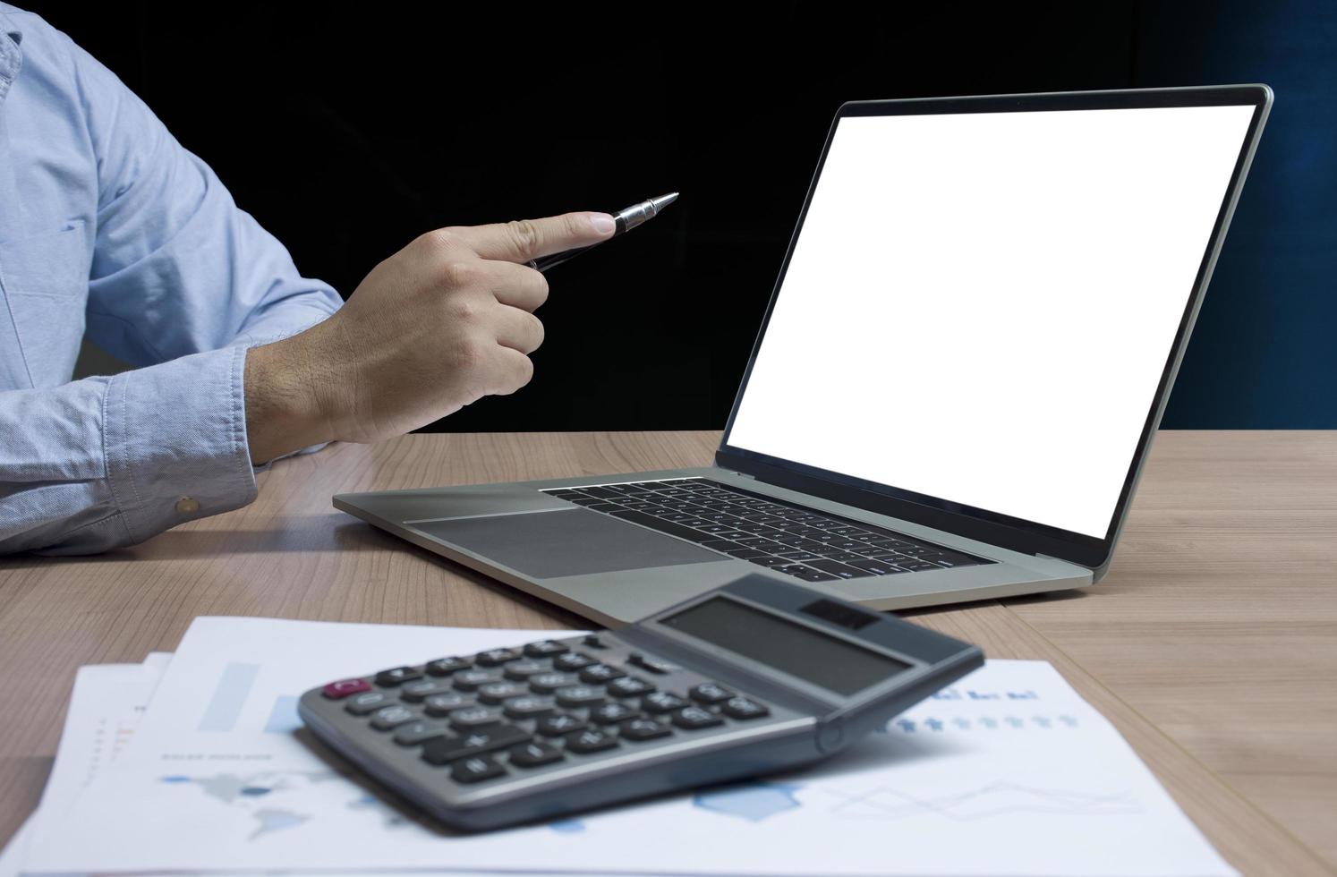 Businessman hand holding pen to display laptop and calculator on table photo